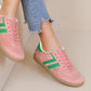 Pink sneakers with green stripes worn by a person on a light background