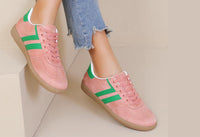 Pink sneakers with green stripes worn by a person on a light background