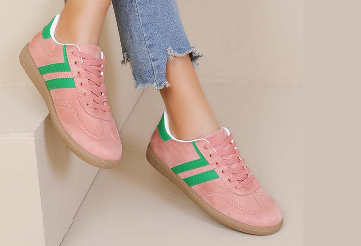 Pink sneakers with green stripes worn by a person on a light background