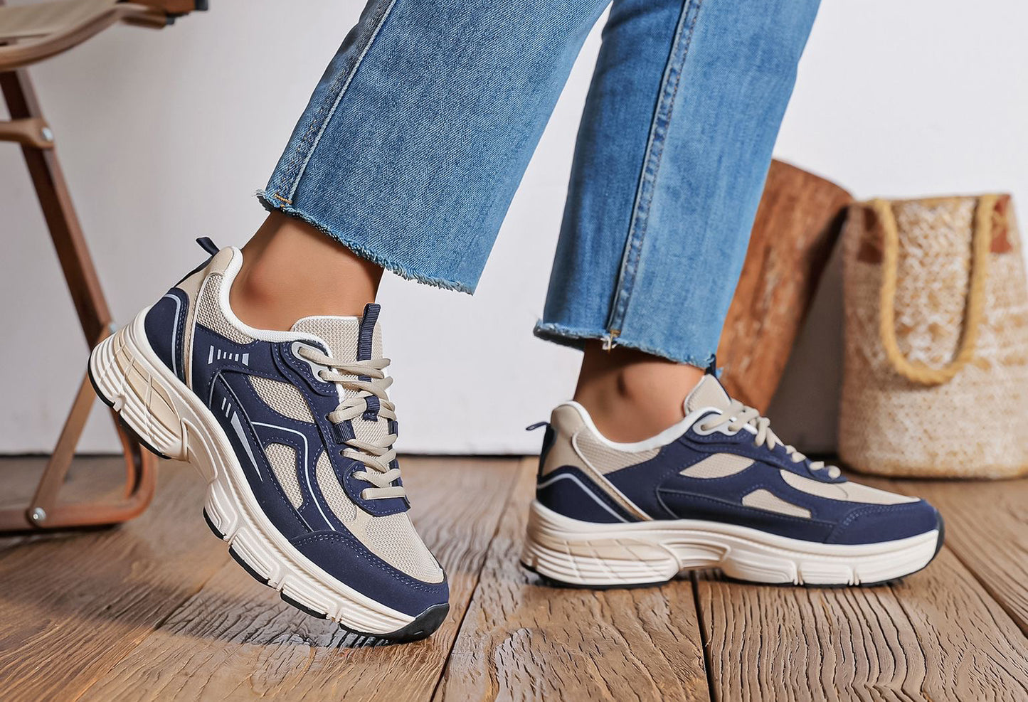Navy and white sneakers worn with blue jeans on a wooden floor.