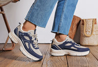 Navy and white sneakers worn with blue jeans on a wooden floor.
