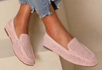 A pair of PINK laser loafer flats worn by a person sitting with crossed legs, showing the soft squared toe slip-on design with a faux suede finish.