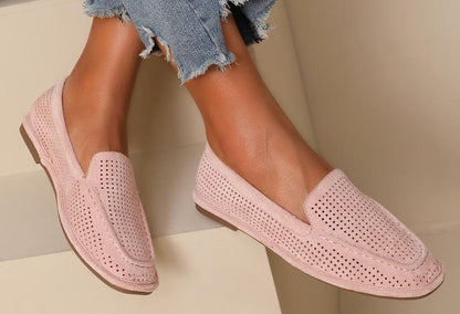 A pair of PINK laser loafer flats worn by a person sitting with crossed legs, showing the soft squared toe slip-on design with a faux suede finish.