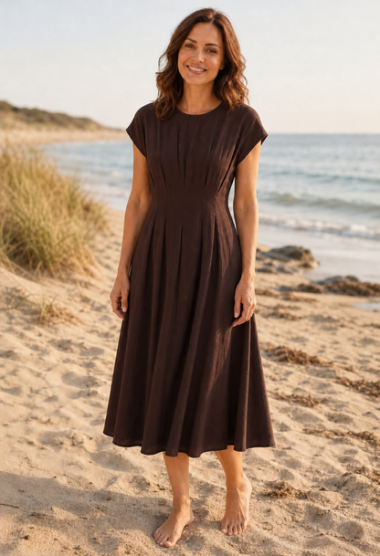 Woman in a brown dress standing on a sandy beach with ocean in the background