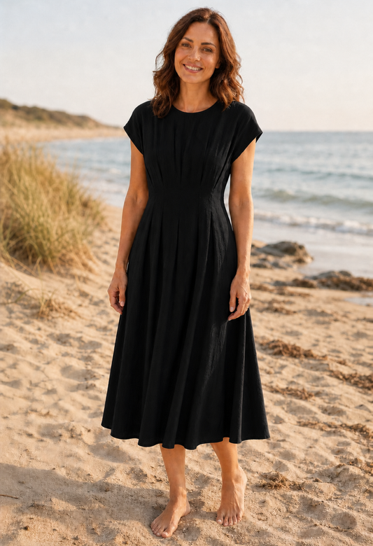 Woman in a black dress standing on a sandy beach with ocean in the background