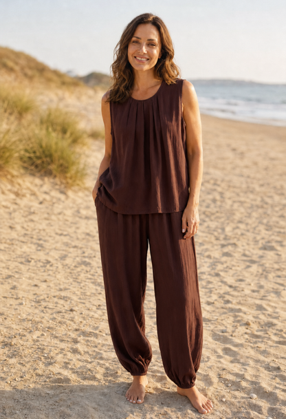 Woman in brown sleeveless top and wide-leg pants standing on a sandy beach.