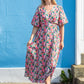 Woman in a floral dress standing against a blue wall