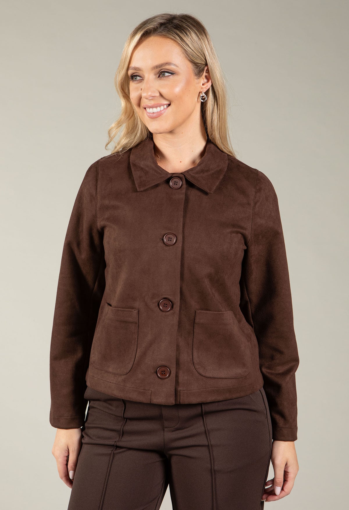 A woman modeling a brown suede-like cropped jacket with a collar, three front buttons, and two front patch pockets.