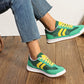 Green and yellow sneakers worn with blue jeans on a wooden floor.