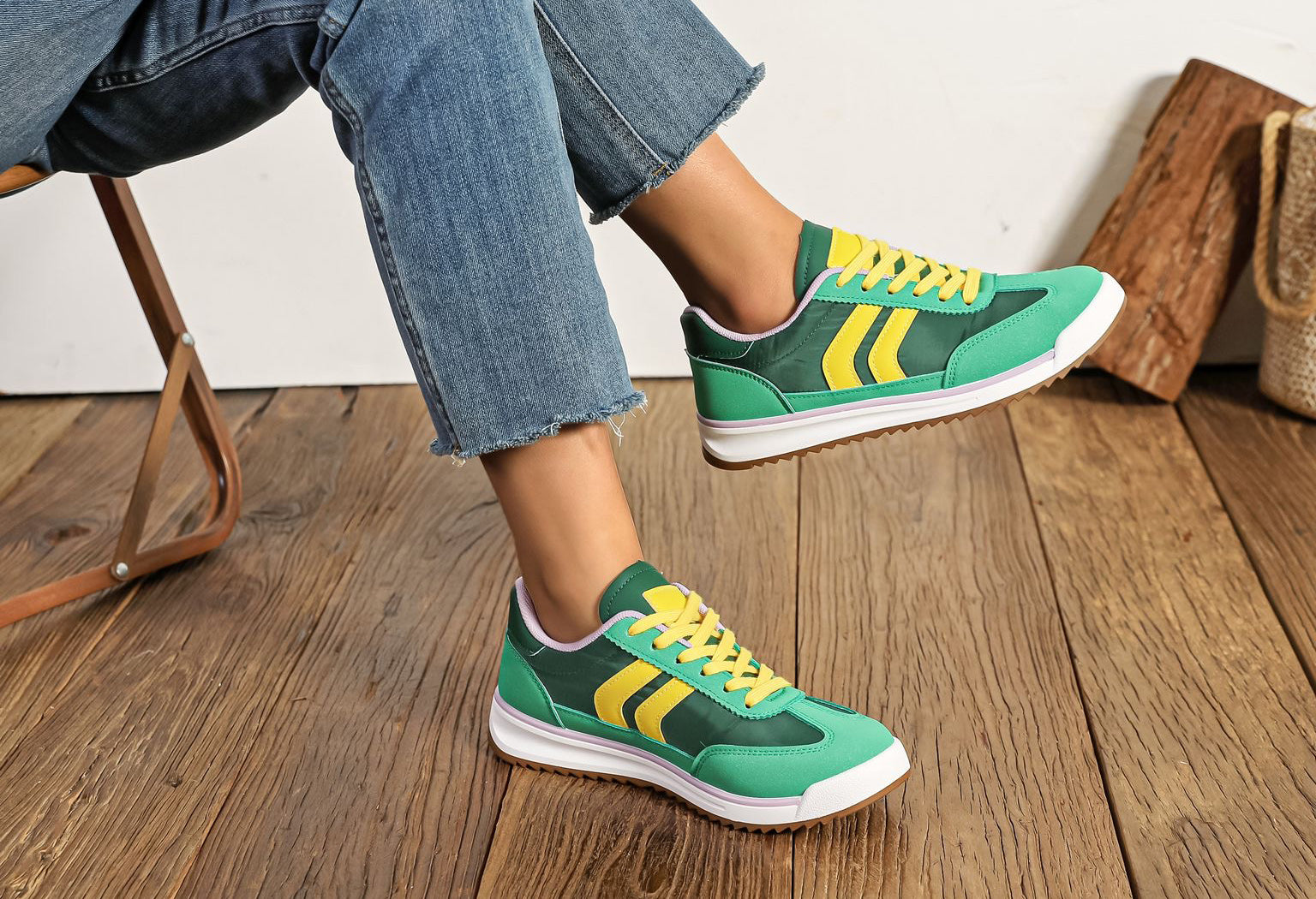 Green and yellow sneakers worn with blue jeans on a wooden floor.