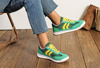 Green and yellow sneakers worn with blue jeans on a wooden floor.