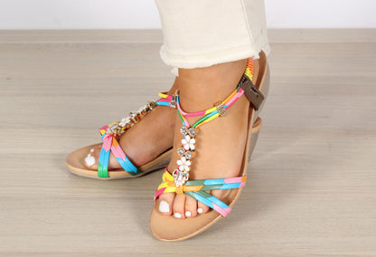 A pair of multi colour open toe sandals with floral and diamond gem embellishments on the straps and a low wedge heel.
