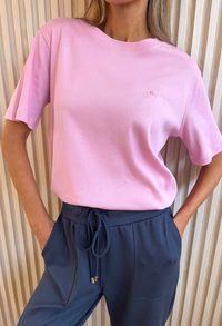 Person wearing a pink t-shirt and blue pants against a neutral background