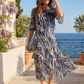 Woman in a patterned dress standing on a balcony with ocean view