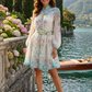 Woman in a floral dress standing by a scenic lake with mountains in the background