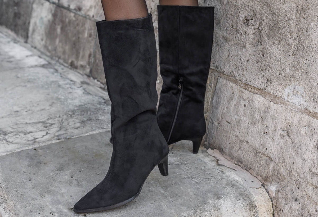 Black knee-high boots worn by a person standing on stone steps.