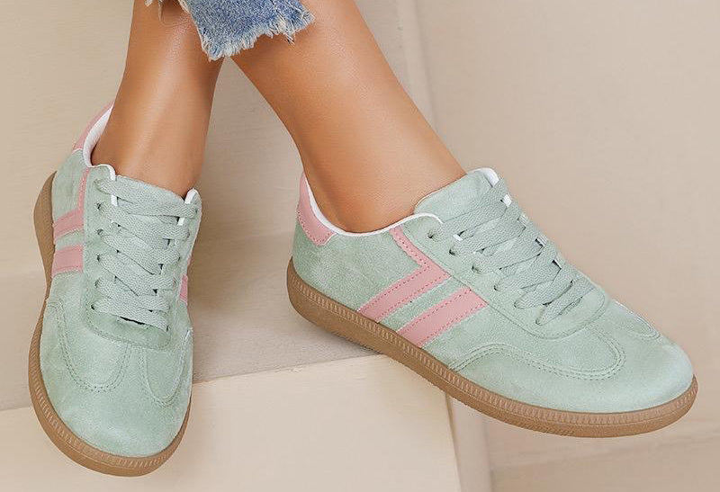Light green sneakers with pink stripes worn by a person on a beige background