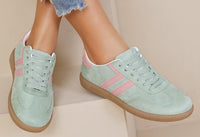 Light green sneakers with pink stripes worn by a person on a beige background