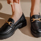 Black loafers with gold accents worn by a person on a beige background