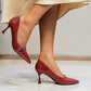 Red high-heeled shoes worn by a person sitting on a chair.