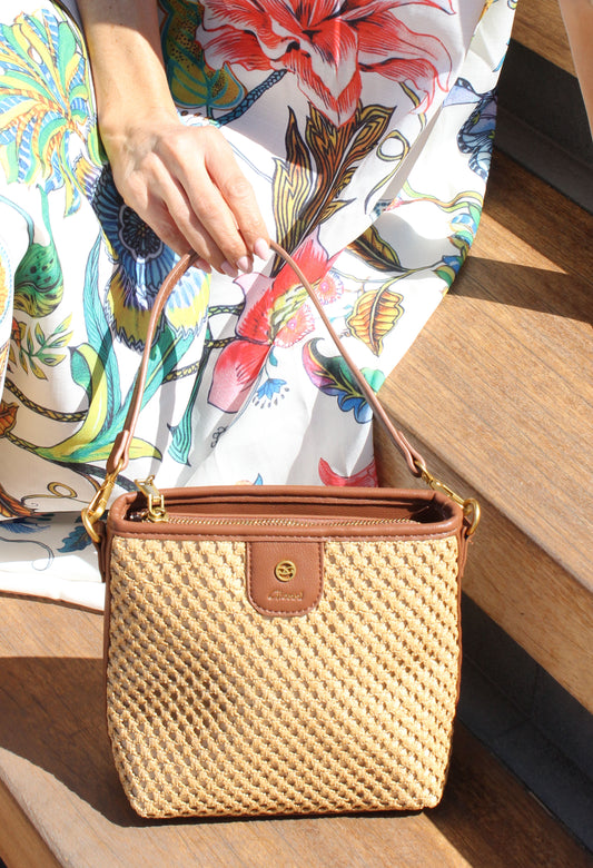 Person holding a woven handbag with a scenic background