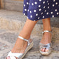 Silver sandals worn with a navy dress with white polka dots on a stone surface.