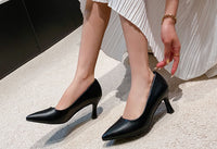 Black high-heeled shoes worn with a light-colored skirt on a neutral background