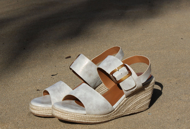 A pair of beige Rochester wedge sandals with a woven effect and padded sole, featuring hook-and-loop straps with an adjustable buckle, placed on a sandy surface.