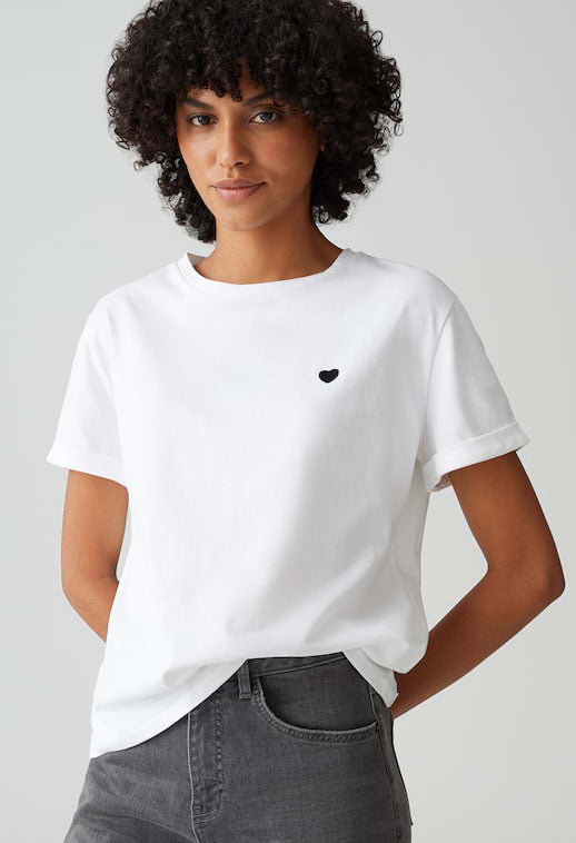 Person wearing a white t-shirt with a black heart design on a plain background