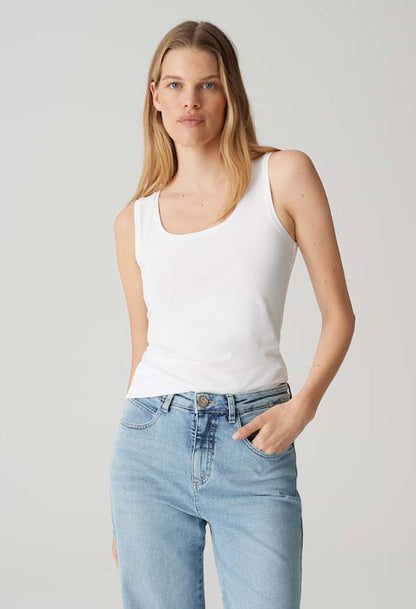 Woman wearing a white tank top and light blue jeans against a plain background