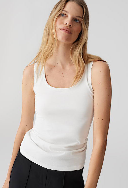 Woman wearing a white tank top against a plain background