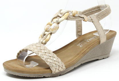 A gold-colored stone beaded wedge sandal with a braided strap and elastic ankle strap on a flat background.