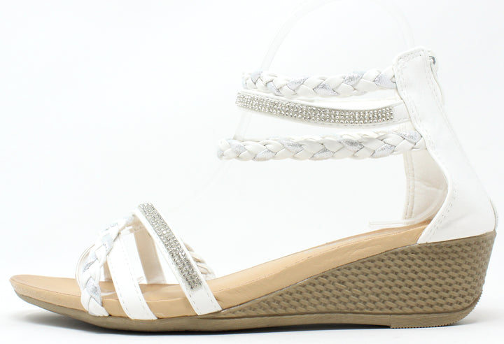 A white-colored wedge sandal with triple ankle straps and a rhinestone-embellished strap across the foot. The sandal features a open toe design and a comfort sole.