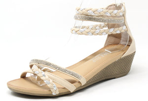 A beige-colored wedge sandal with triple ankle straps and a rhinestone-embellished strap across the foot. The sandal features a open toe design and a comfort sole.