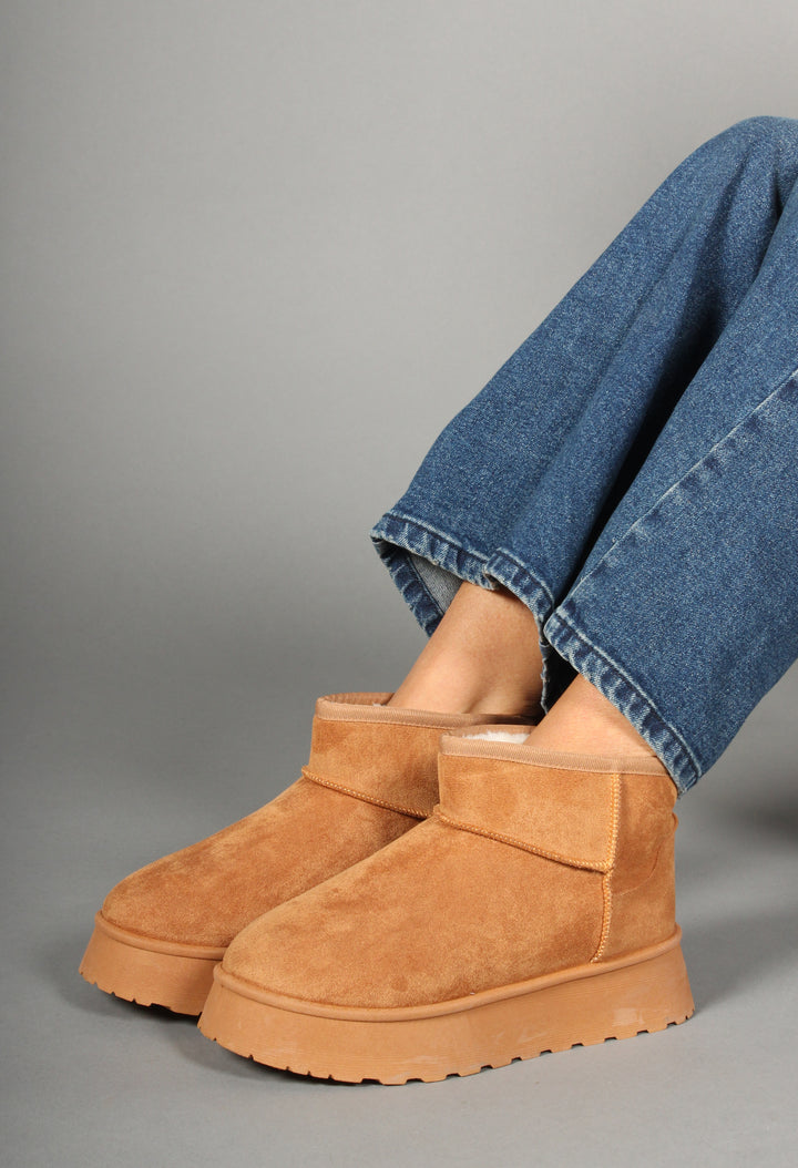 A woman is seated wearing camel faux fur lined platform boots with a round toe design.