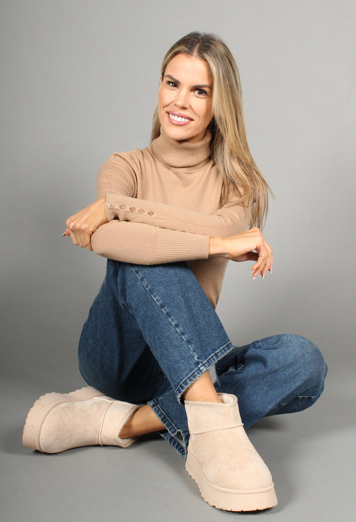 A woman is seated wearing beige faux fur lined platform boots with a round toe design.