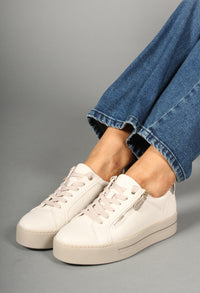 White sneakers worn with blue jeans on a gray background