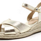 A metallic gold espadrille sandal with adjustable ankle strap and cross straps at the toe, featuring a wedge heel.