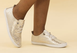 A pair of gold and white leather plimsolls with a metallic leopard print and whip stitched detail.
