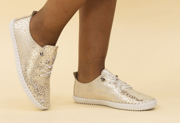 A pair of gold and white leather plimsolls with a metallic leopard print and whip stitched detail.