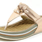 A rose gold colored sandal with a thong style strap and a flat sole.