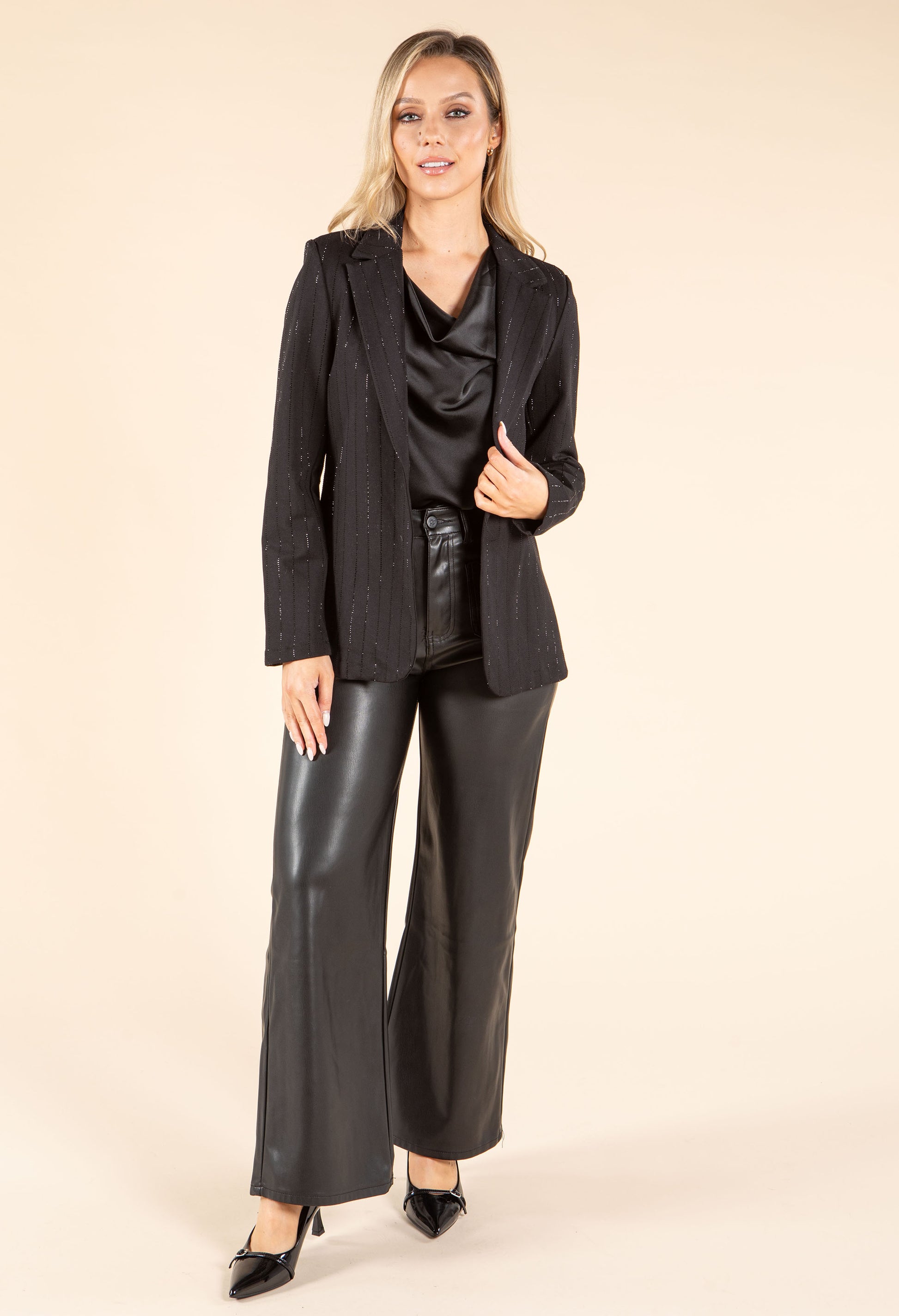 Woman wearing a black outfit with a jacket and leather pants on a beige background