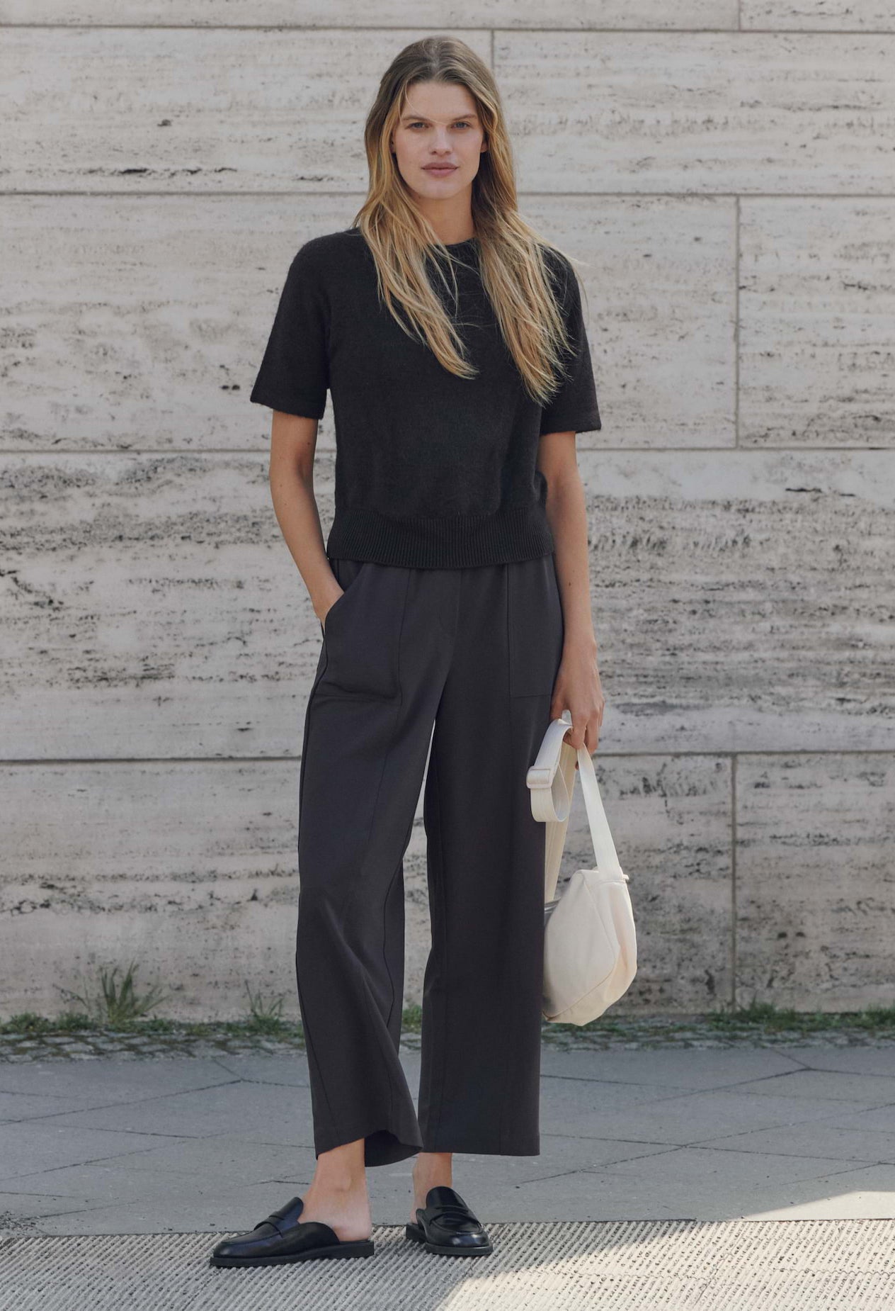 Woman wearing a black outfit standing against a textured wall.