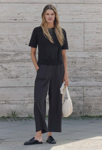 Woman wearing a black outfit standing against a textured wall.