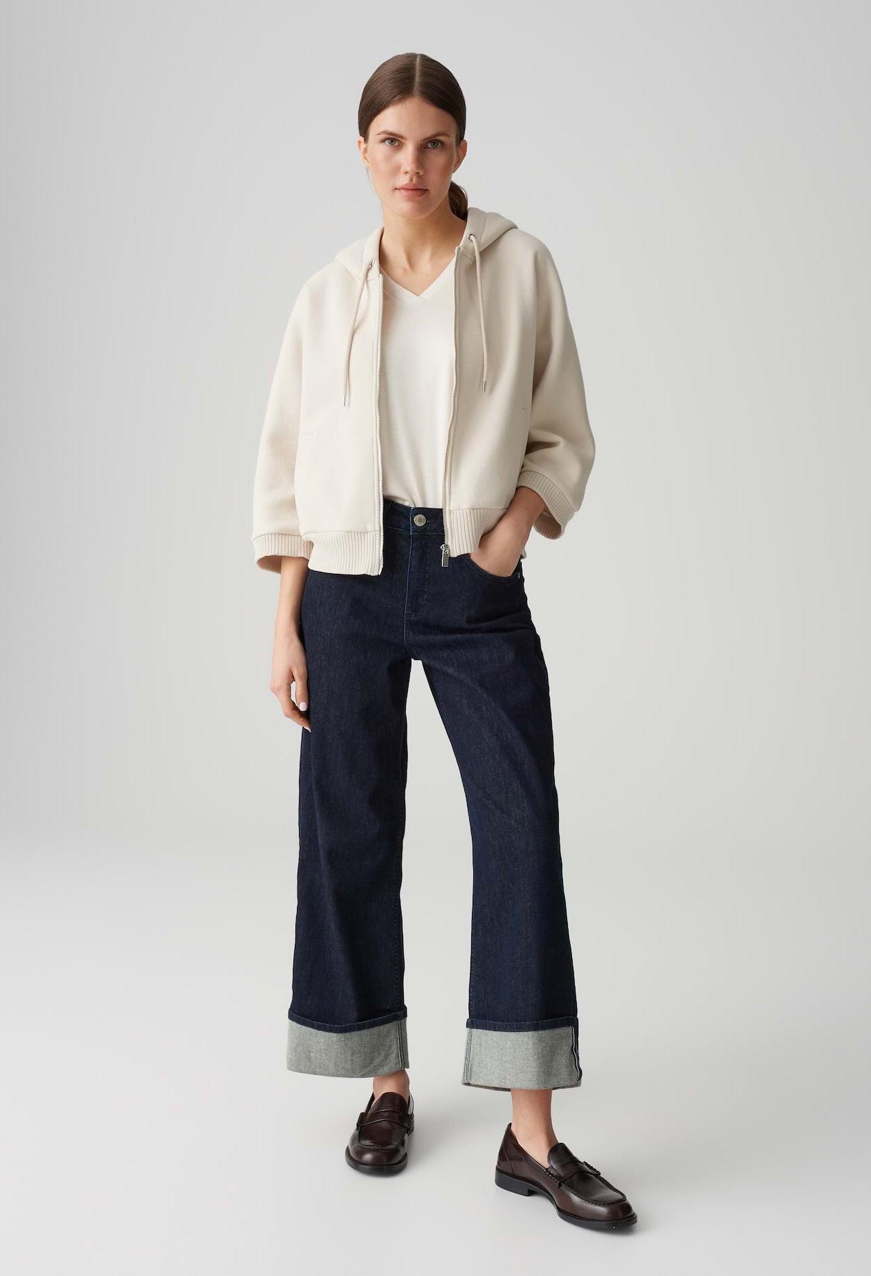 Woman wearing a beige jacket, white shirt, and dark blue pants on a light gray background