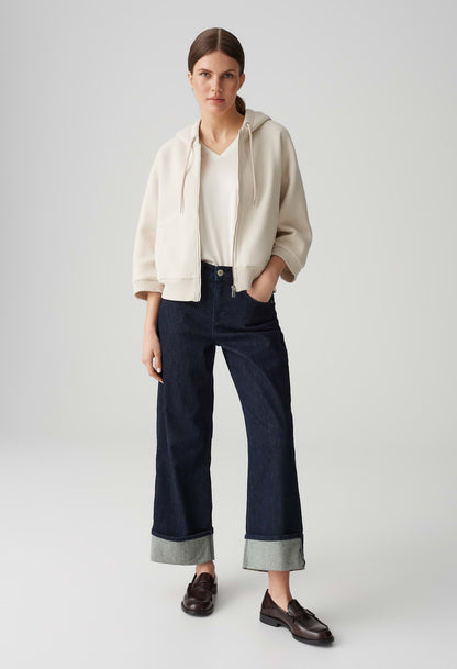 Woman wearing a beige jacket, white shirt, and dark blue pants on a light gray background