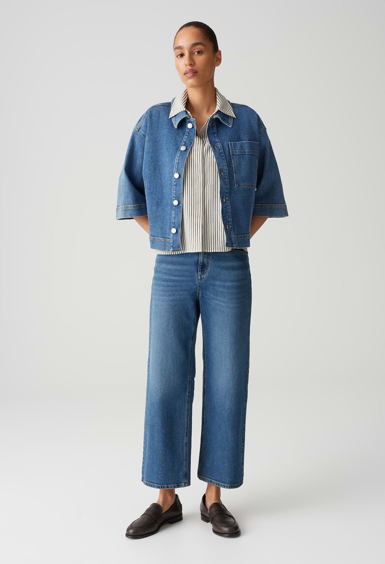 Person wearing a denim jacket, striped shirt, and jeans on a white background