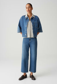 Person wearing a denim jacket, striped shirt, and jeans on a white background