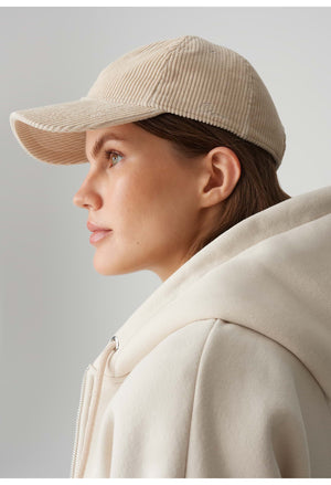 Woman wearing a beige cap and coat against a plain background