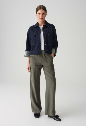 Person wearing a navy denim jacket, white shirt, and olive green pants on a light gray background